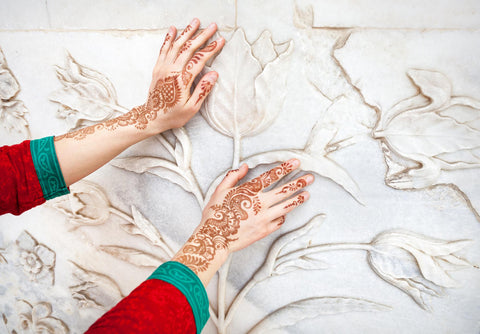 A woman touching wall art with floral henna designs on the back of her hands.