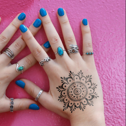 Hand With Blue Nails and Mandala Tattoo Adorned With Rings.