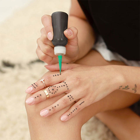 A woman adorning her fingers with Jagua temporary tattoos using an applicator bottle.