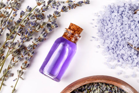 A photo of a lavender essential oil surrounded by lavender flowers.
