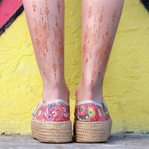 A woman displaying a ruma henna tattoo with intricate patterns on her legs