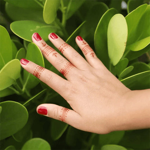 A woman’s fingers adorned by wren henna tattoos.