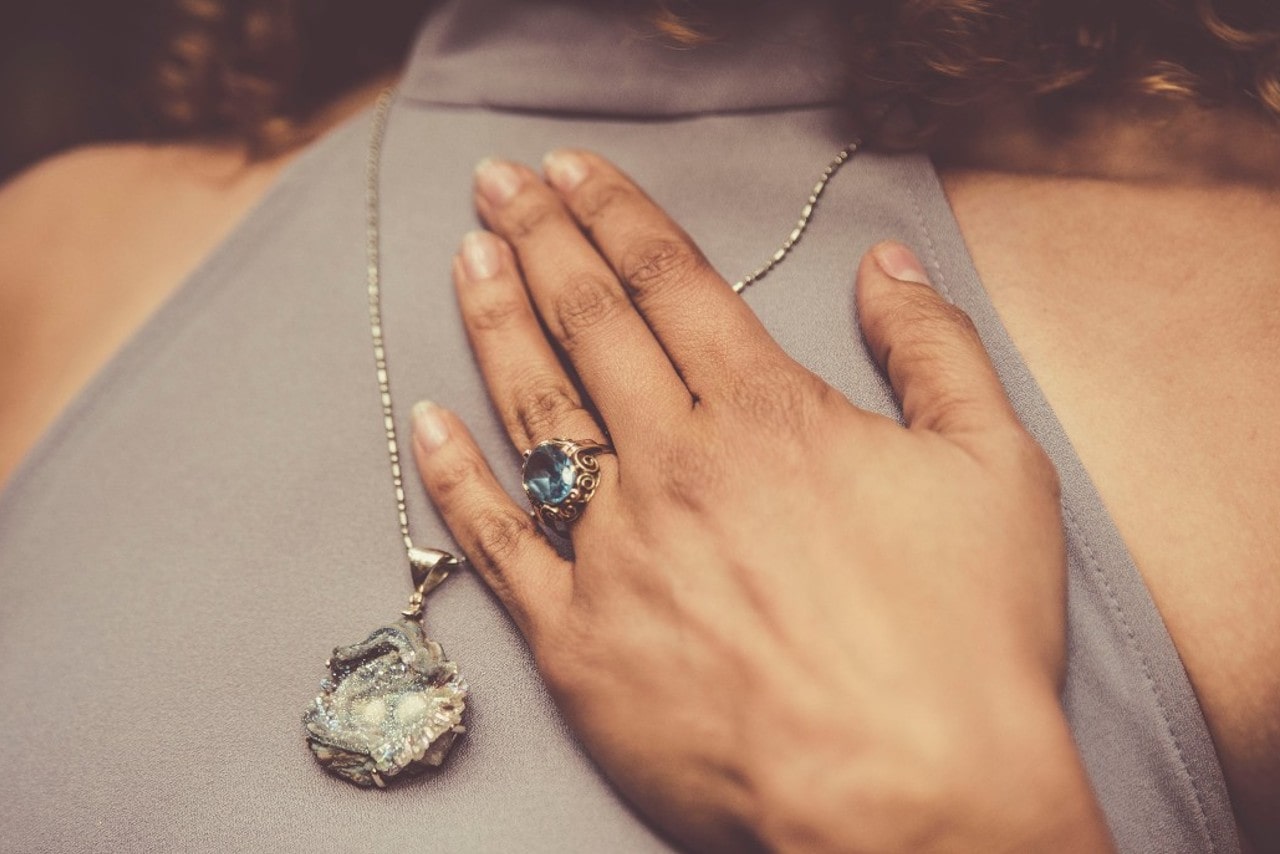 Lady wearing a blue topaz fashion ring with filigree and a gemstone necklace