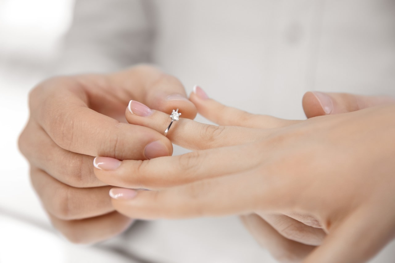 A person putting a solitaire diamond engagement ring on a woman’s hand