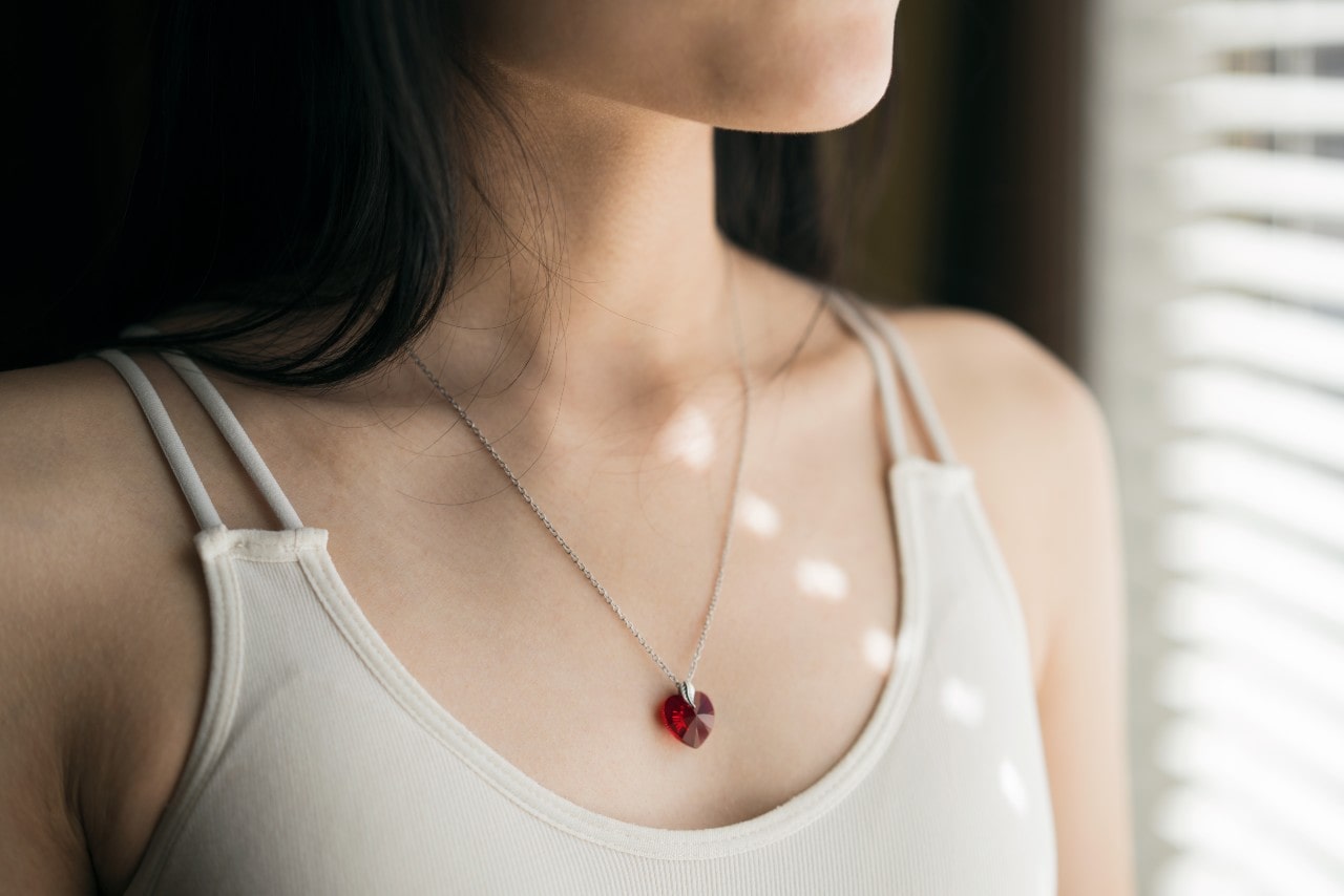 A woman wearing a ruby heart gemstone pendant stands in front of the window.