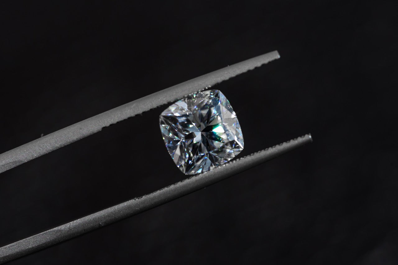 A cushion cut diamond held between tweezer