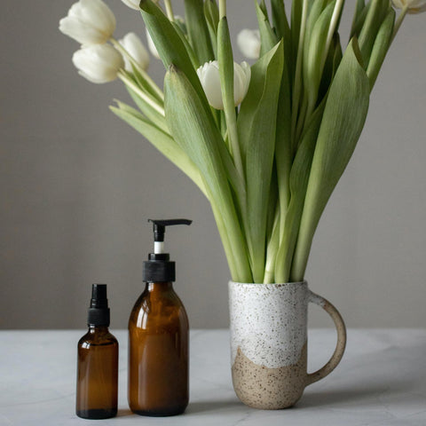 Brown natural skincare products next to a vase of white roses