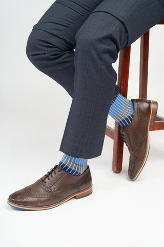 Man sitting on a chair wearing brown shoes, blue Chord socks from Peper Harow and a navy suit