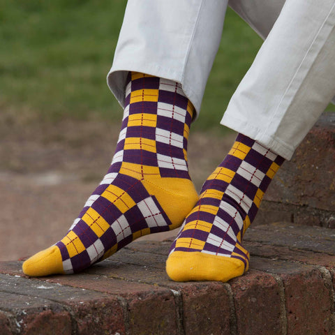 Man wearing white business casual trousers and Peper Harow Checkmate gold luxury socks sitting on a wall