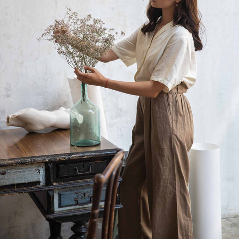 Woman wearing linen shirt and trousers adjusting flowers.