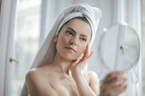 Woman with a towel on her head looking into a mirror