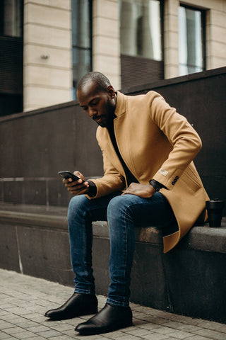 Man sitting wearing a trench coat looking at his phone, credit to Cottonbro Studio on pexels