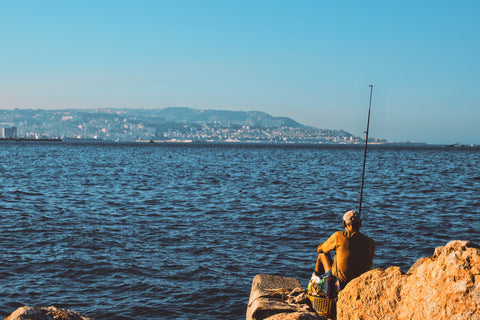 A man sitting on a rock fishing.