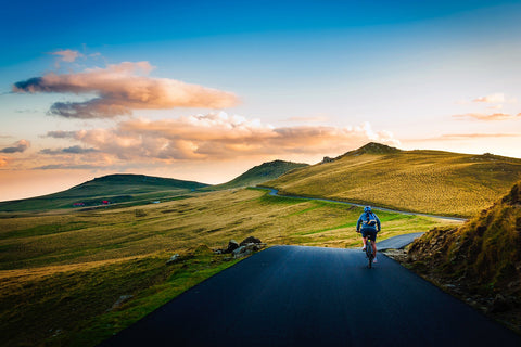 Man cycling on a road with a scenic background of hills.