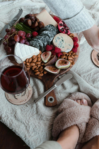 A tray of gourmet food snacks and glass of wine, alongside a girl wearing slippers
