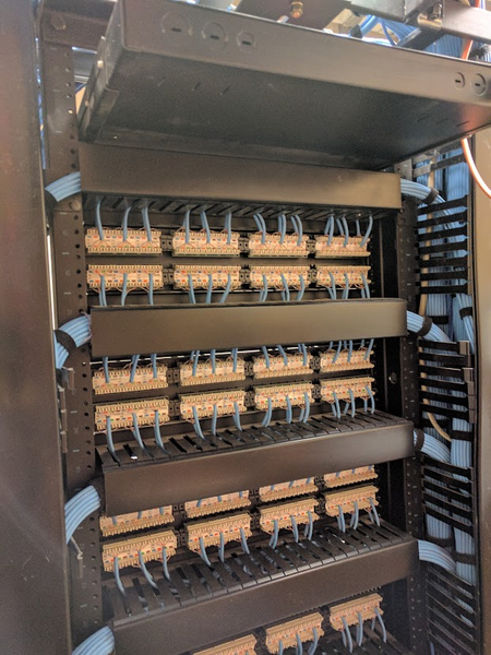 A view of the rear of a telecommunications rack in a commercial setting equipped with multiple punch-down patch panels.