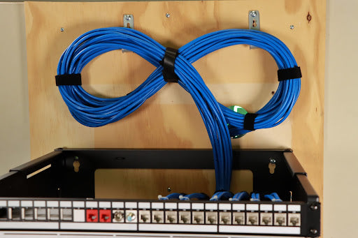 A pair of blue cables hanging from a wooden wall next to a patch panel.