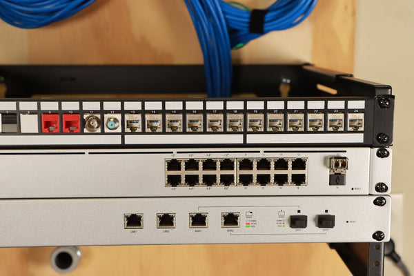 Image of a computer on a shelf with a Ubiquiti UniFi Switch USW-24-POE. The computer is connected to the switch with an Ethernet cable. The text "Ubiquiti UniFi Switch USW-24-POE" is visible on the switch.