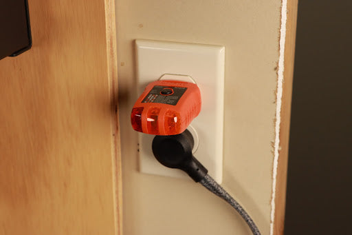 An AC power outlet with a three-prong plug inserted. The plug is connected to a power cord that is plugged into the outlet.