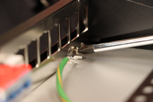 Closeup of a person using a screw driver to connect the ground wire to a patch panel.