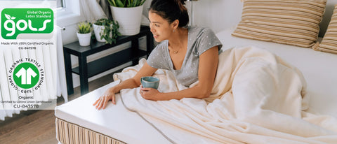 Woman smiling on an Essentia organic mattress showing GOLS and GOTS certifications