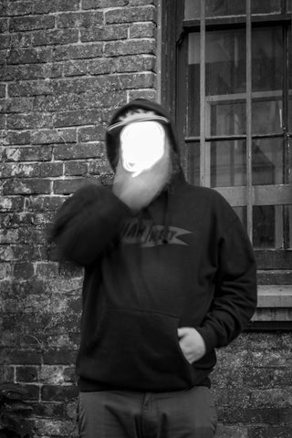 A person who's face appears missing due to added light in front a brick wall.