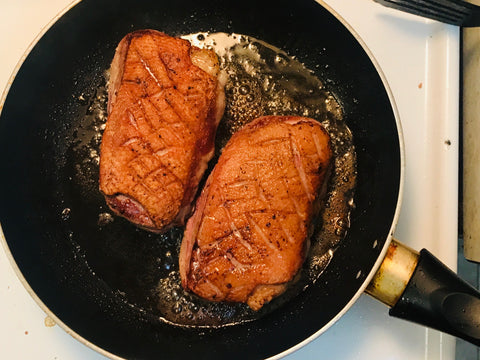 Two scored duck breasts cooking in a pan