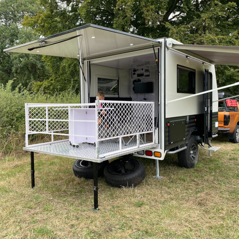 Picture of the caravan with the back open and porch set up with team member sat on