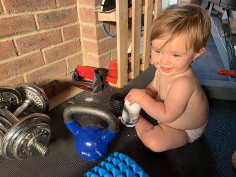 Baby Arla sitting next to weights in the gym