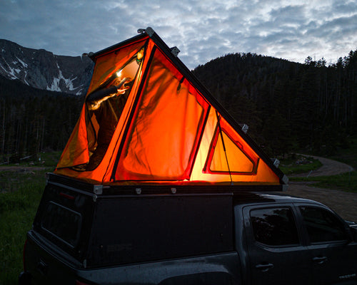 Light showing through the GF Platform Camper tent, with a person inside and the rear door open