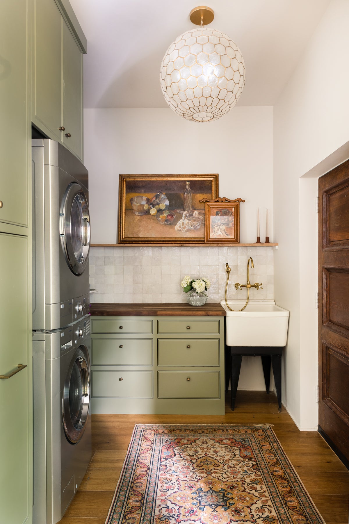 White zellige tile on a laundry room backsplash, behind green cabinets and an antique sink.