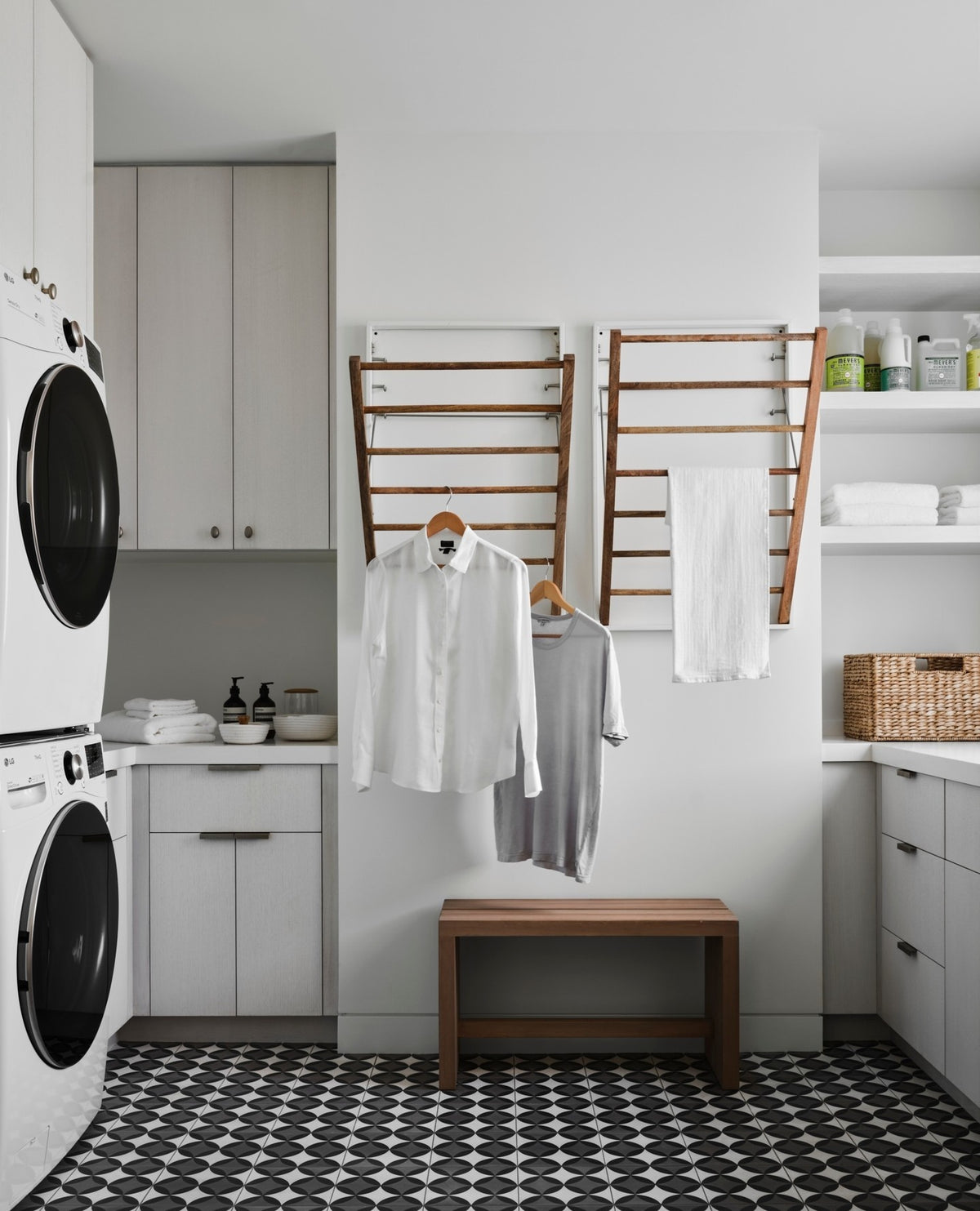 A laundry room with a black and white tiled floor, white walls and fold down wooden laundry racks.