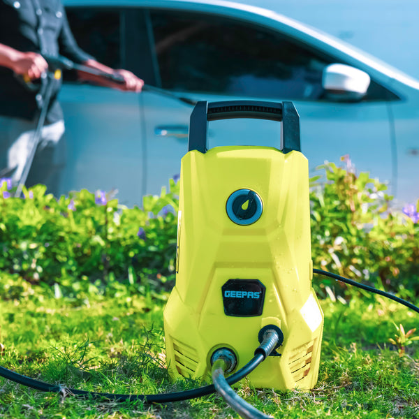 The yellow pressure washer being used to clean a car, the pressure washer is placed on the front is on the grass patch in the front garden.
