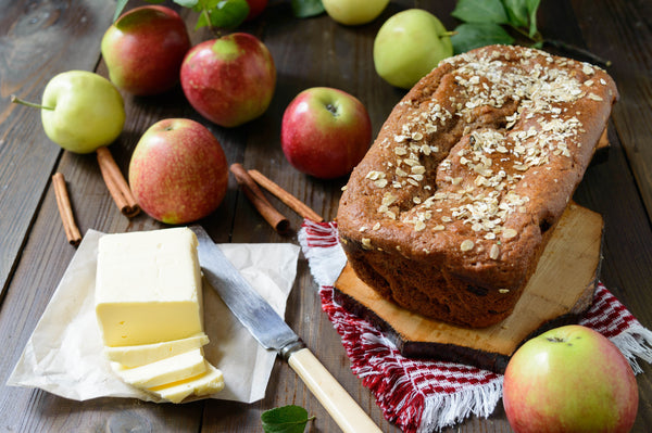 Apple cinnamon bread loaf on a wooden chopping board along with apples and butter besides it.