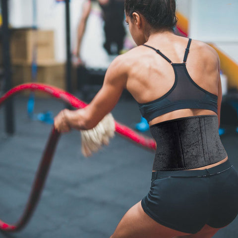 Female athlete wearing a back brace using battle ropes