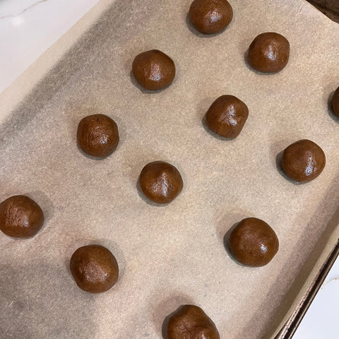 Gingersnap cookies rolled into a balls on a baking sheet lined with parchment paper