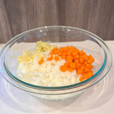 Sliced carrots and white onions in a transparent bowl.