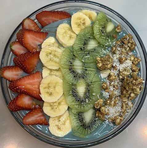 A bowl full of fruits, strawberries, bananas, kiwis, granola and blue spirulina smoothie.