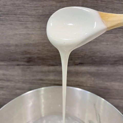 Wooden spoon pouring vanilla extract into a bowl.