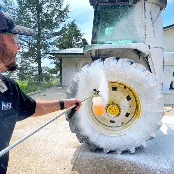 Image Wash Product employee foaming a John Deere with a pressure washer foam cannon