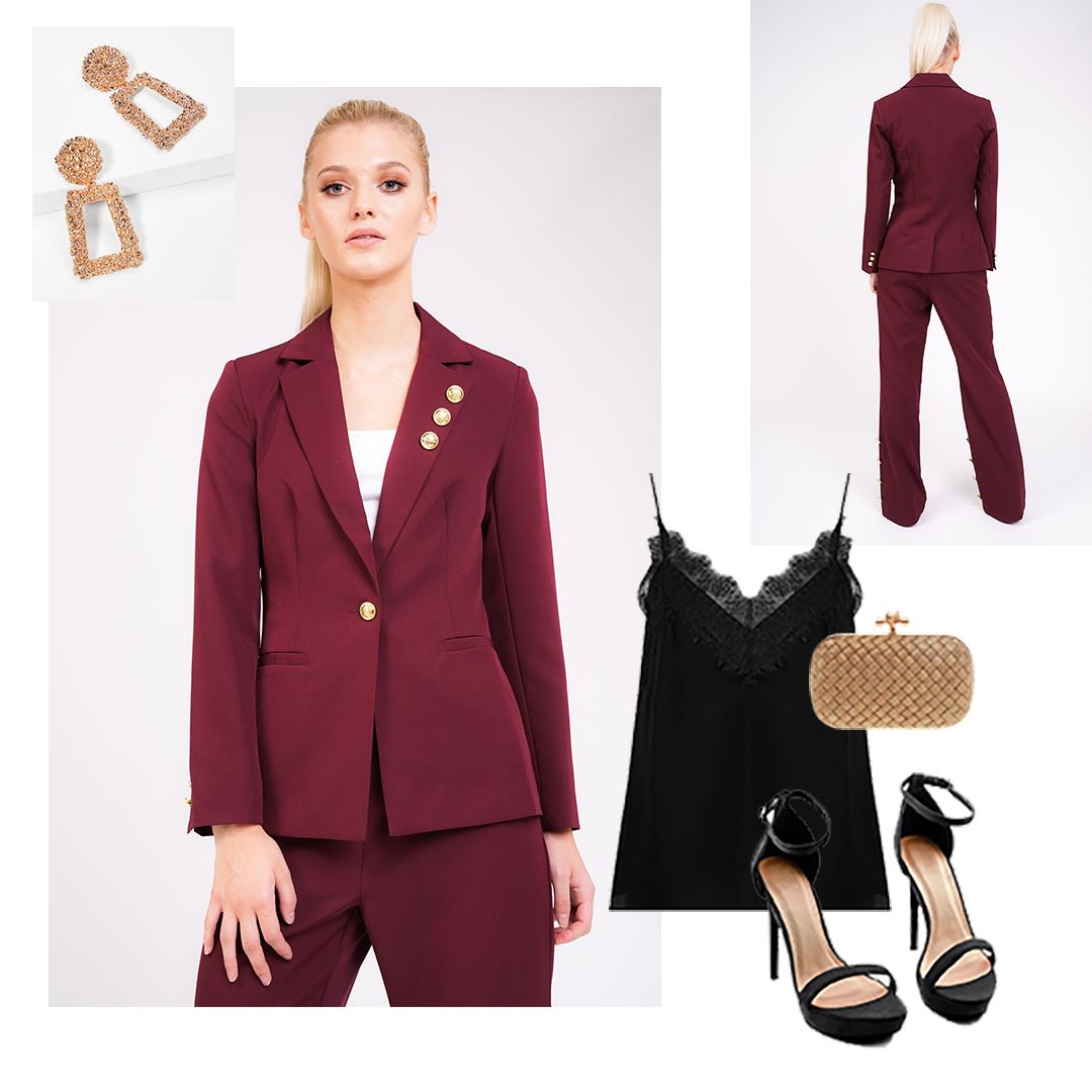 Model wears deep red tailored blazer and trouser suit with gold button detail on collar, cuff and front fastening