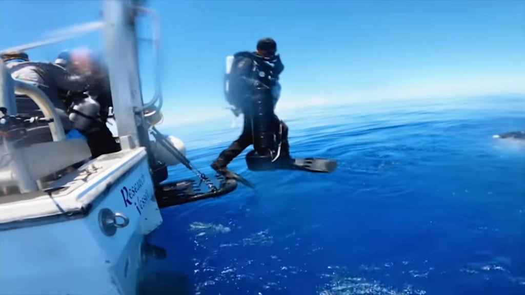 diver jumps off boat into water, carrying a CudaX DPV