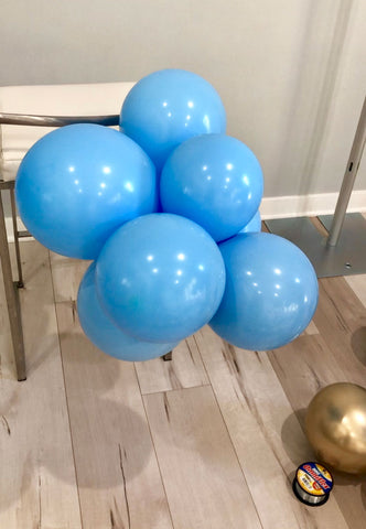 A stack of multiple light blue balloons tied together and tied to the post of a chair.