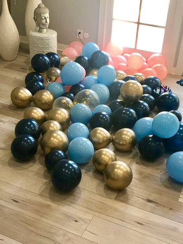 Dark and light blue, pink and gold balloons blown up laying on the floor.