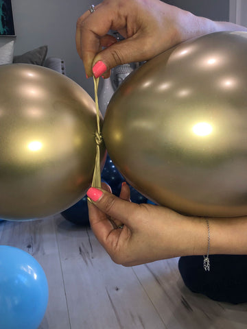 Two gold balloons being tied together by their knots.