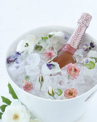 A bottle of sparkling rosé in a white ice bucket with floral ice cubes.