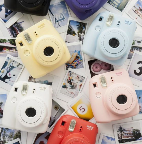 Various colors of polaroid cameras laying on top of polaroid pictures. 