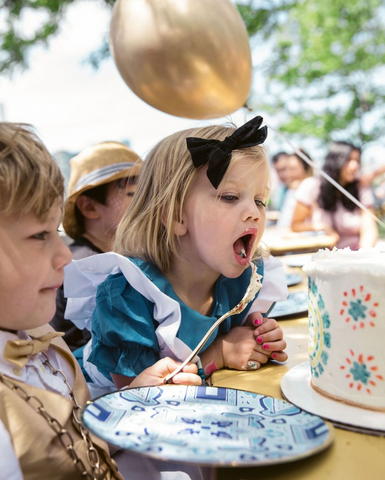 Little girl eating birthday cake. Dressed in Alice in Wonderland with party decor plates.
