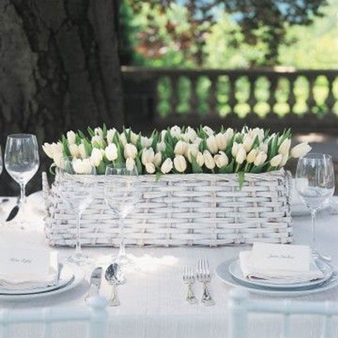 Gray whicker basket filled with white tulips and greenery. Simple white place settings and silverware.