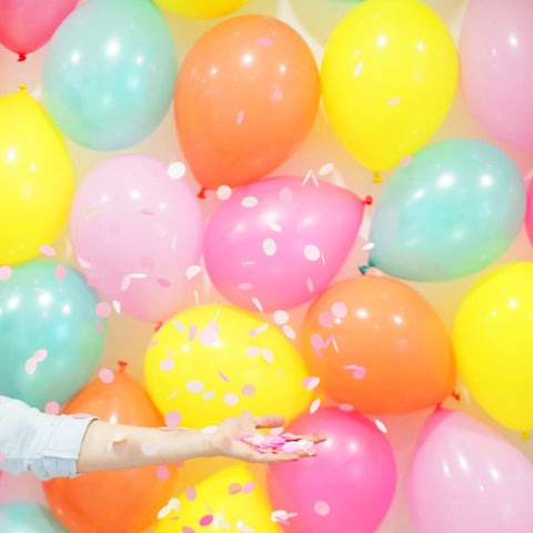 Pastel colored ballons with a girl throwing pink confetti.